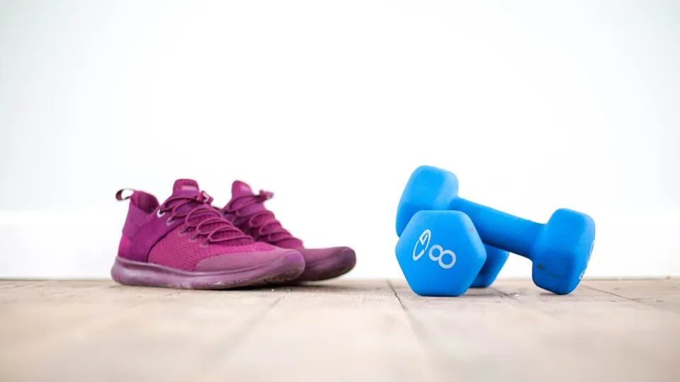 Pink sneakers and blue dumbbells on a wooden floor