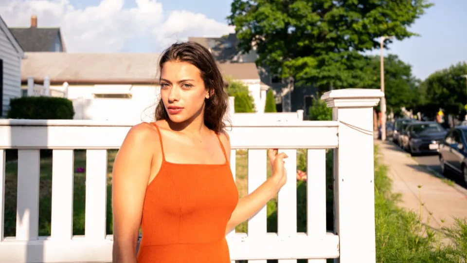 Woman in an orange top standing by a fence